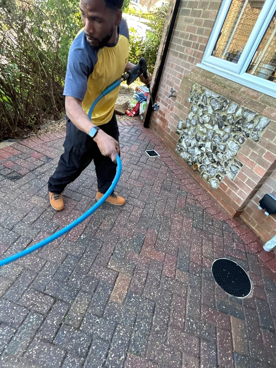 A worker with a hose cleaning a block-paved driveway