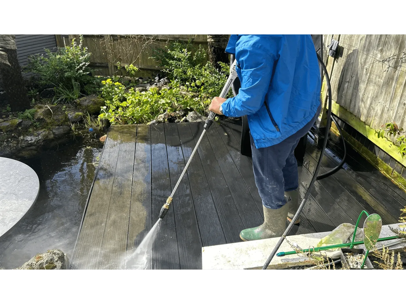 An operative pressure washing garden decking beside a pond